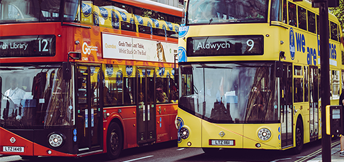 Iconic red and yellow double-decker buses on a London street, with the nearest bus heading towards Aldwych.